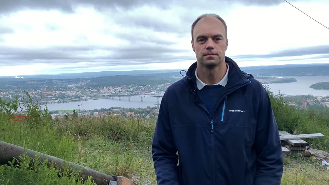 Man står utomhus med en stad i bakgrunden.