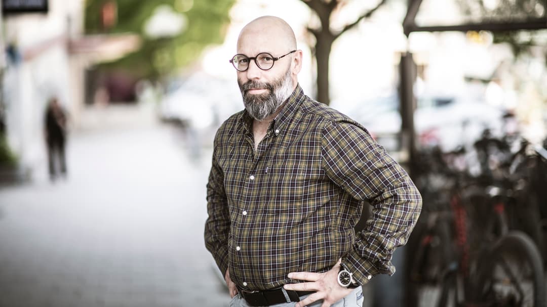 Man med rutig skjorta ler mot kameran