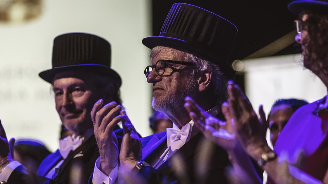 Four well-dressed people with doctor's hats clap their hands.
