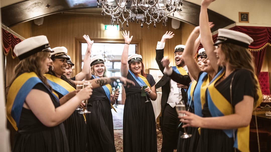 En grupp glada ungdomar med studentmössor jublar med en hand i luften.