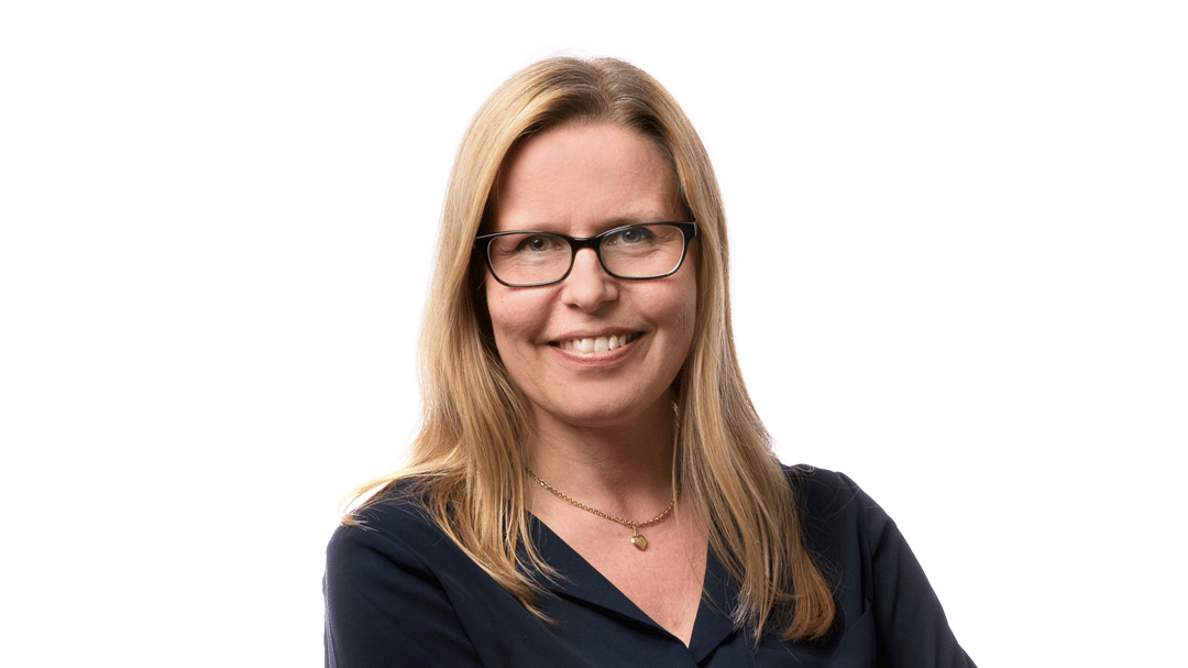 Woman with light hair, glasses and dark blouse and skirt.