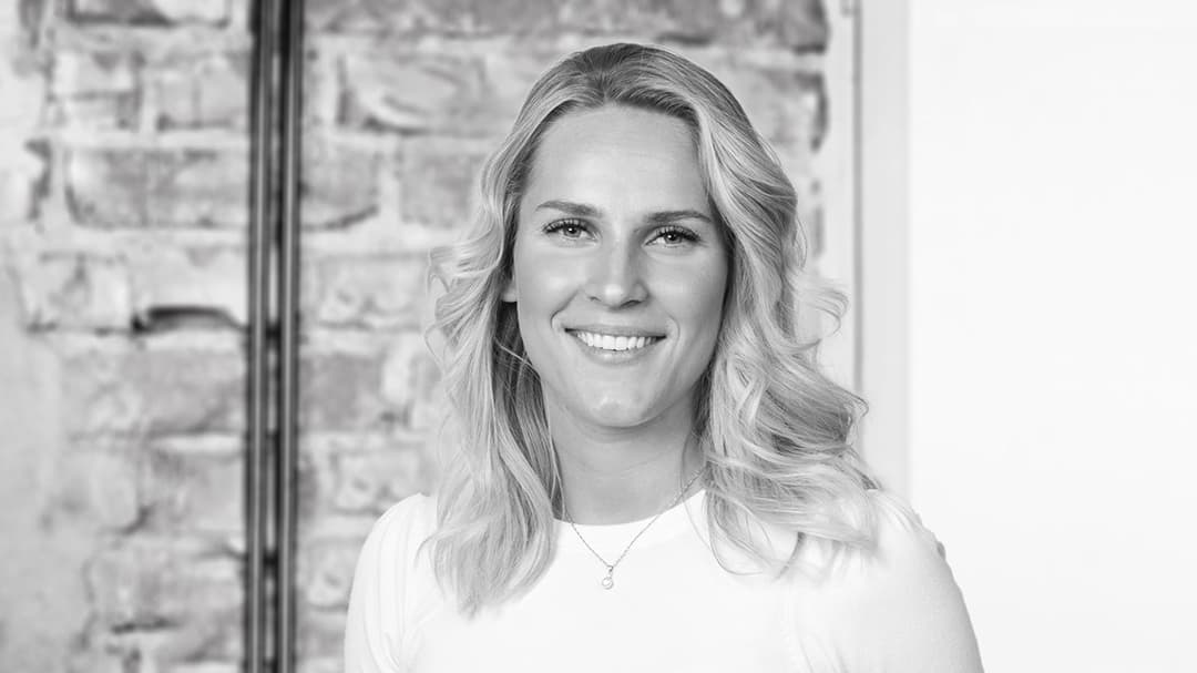 Kvinna med ena handen i fickan som står framför en tegelvägg