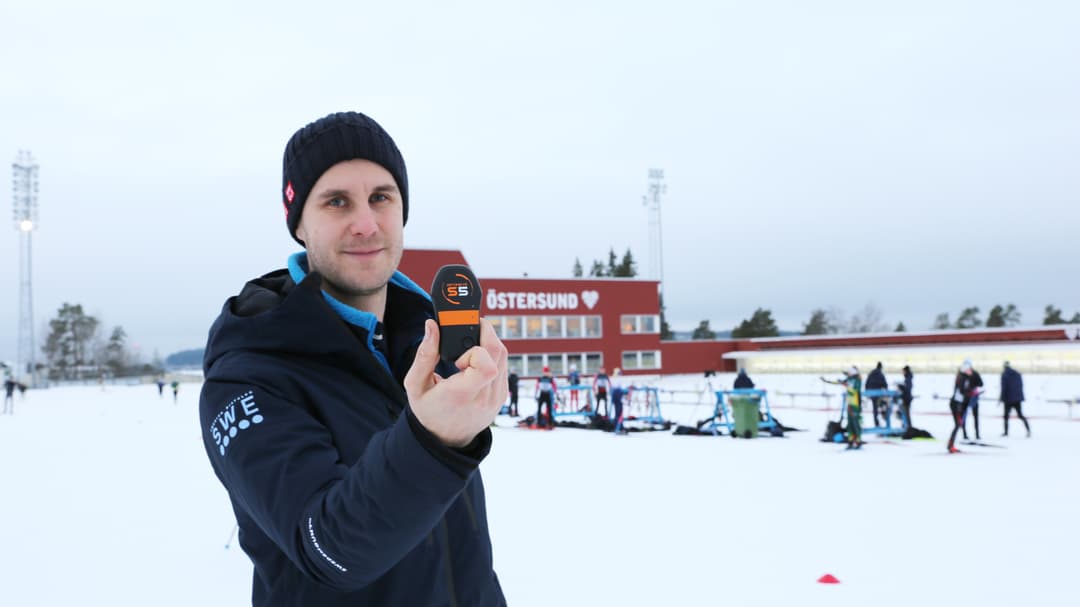 Man som visar upp en sensor stående utomhus i på en skidskyttestadion i vinterlandskap.