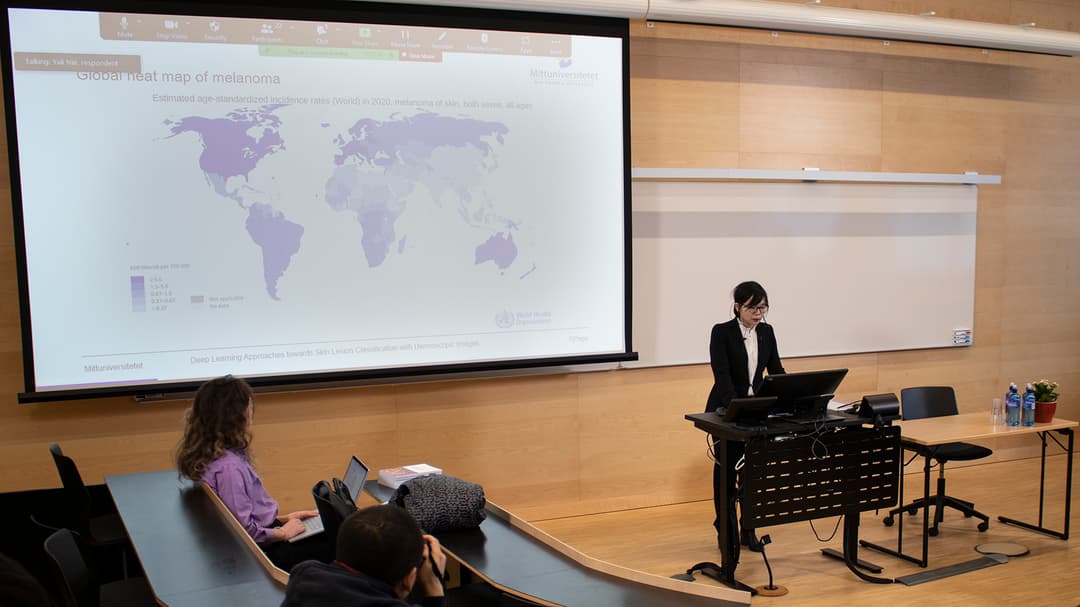 A person gives a presentation, on a large screen a picture is displayed, depicting a map of the world.