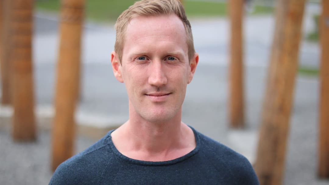A man with dark blue sweater, wooden logs visible in the background