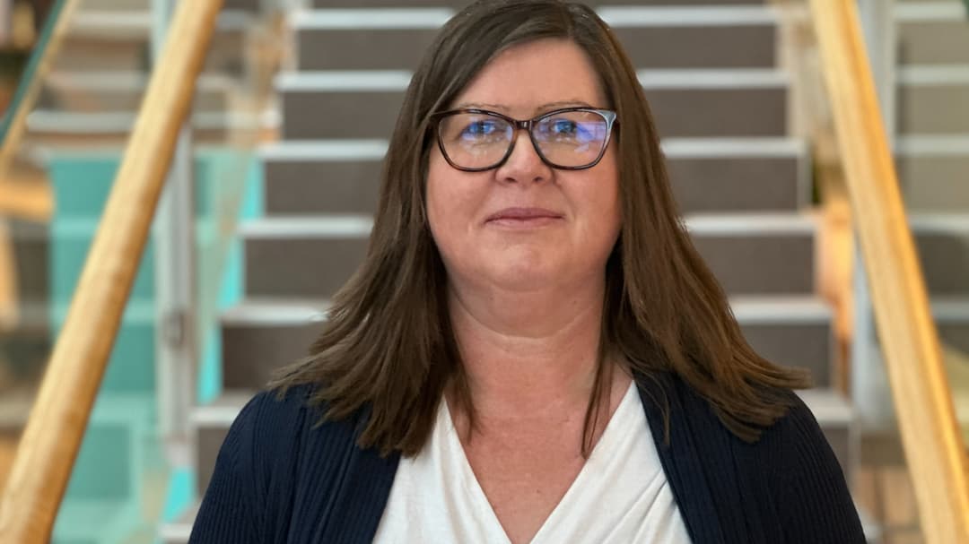 En kvinna med brunt hår står framför en trappa