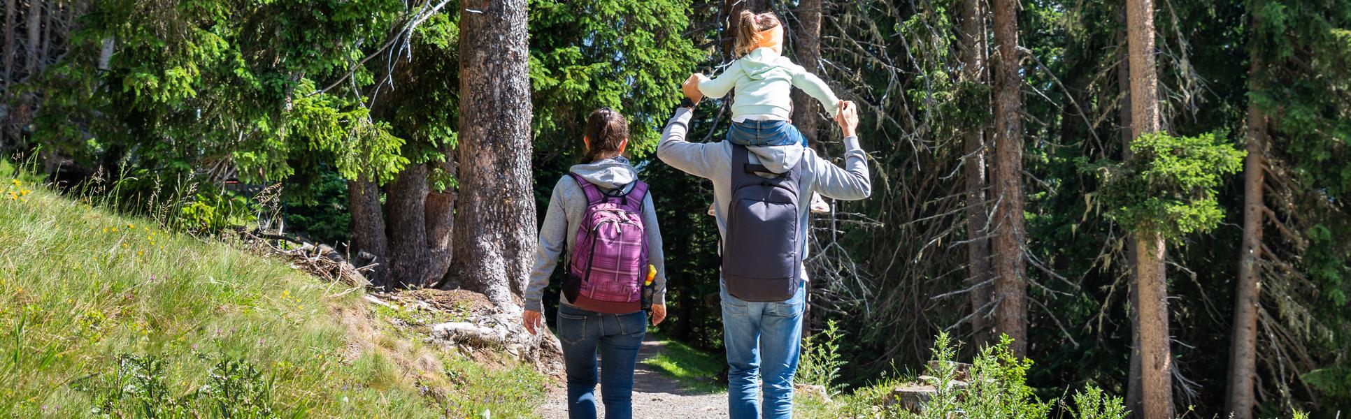 kvinna med ryggsäck  och man med barn på axlarna vandrar i skogen