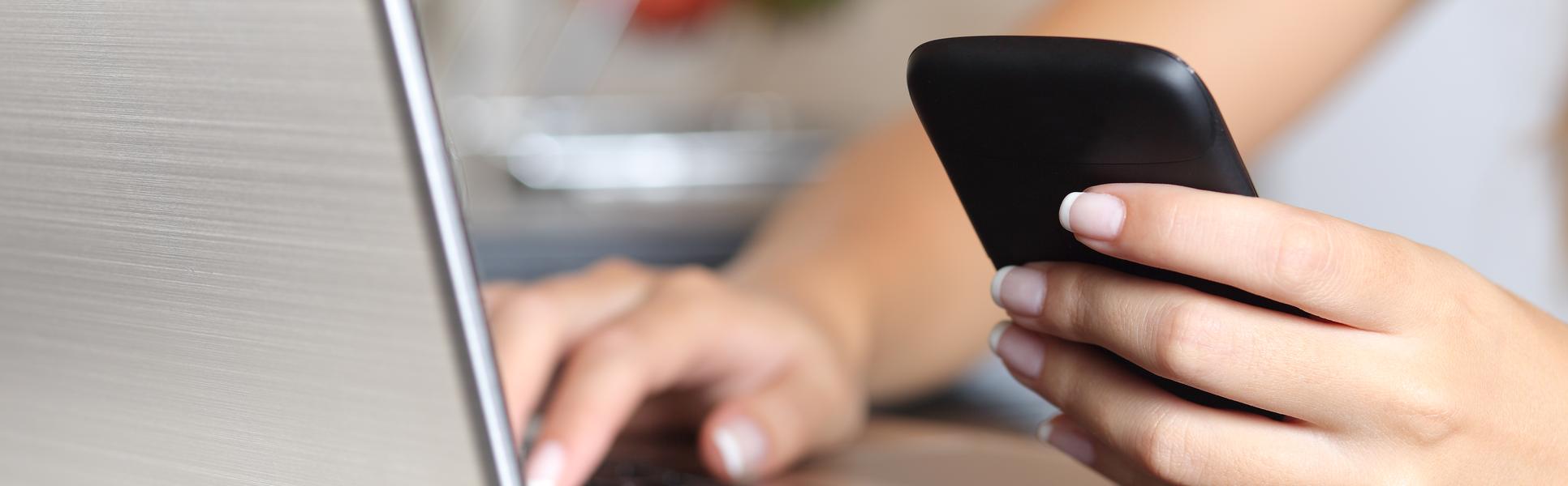 9994506-woman-hand-using-a-smart-phone-and-typing-a-laptop-at-home.jpg