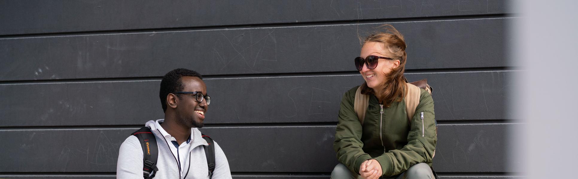 Två studenter som sitter på gul bänk. 