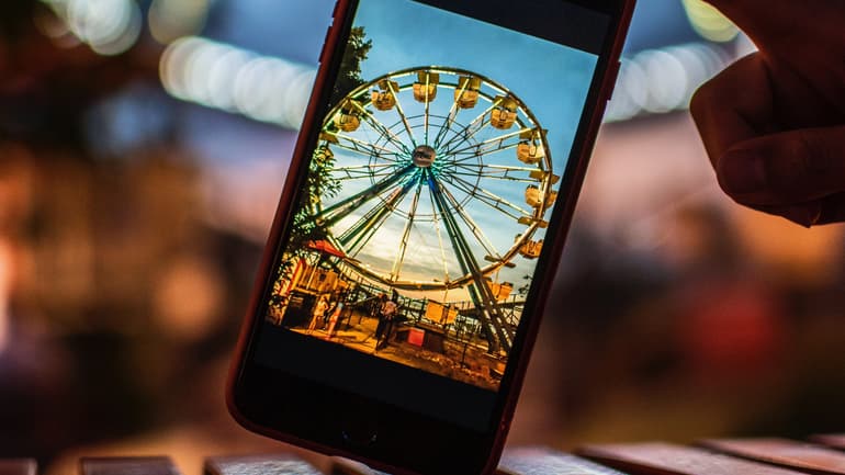 Metabild: Person tar en bild på ett Pariserhjul med mobilen och ser motivet både i mobilen och i verkligheten