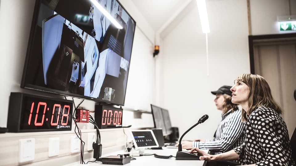 Två personer sitter vid ett långt arbetsbord. Framför dem finns flera datorskärmar, mikrofon och annan teknisk utrustning.