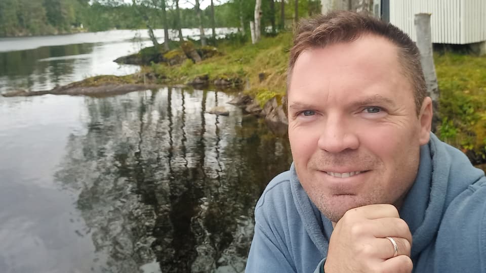 En man sitter vid ett vattendrag, lutar hakan mot handen
