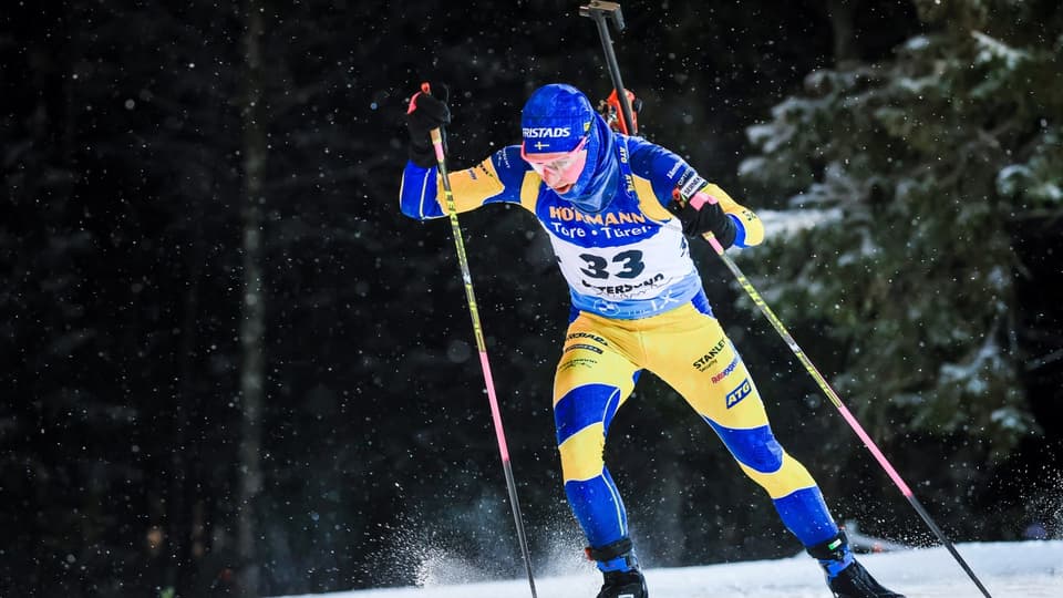 Skidskytt i svensk landslagsdress och med gevär på ryggen