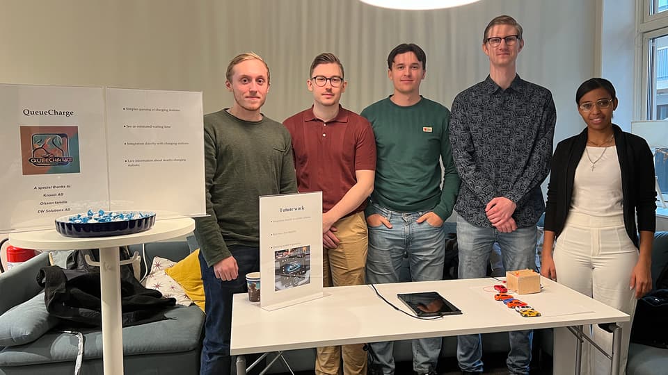 Five people stand behind a table where a prototype of a virtual queue system for electric car chargers is located.