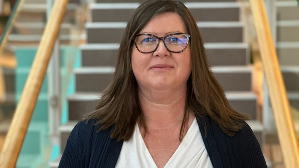 En kvinna med brunt hår står framför en trappa