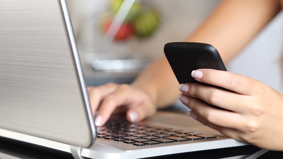 9994506-woman-hand-using-a-smart-phone-and-typing-a-laptop-at-home.jpg
