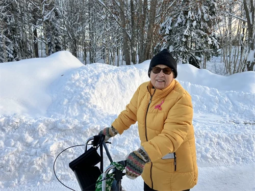 Glad äldre kvinna iklädd varma vinterkläder är ute och promenerar med sin rullator.