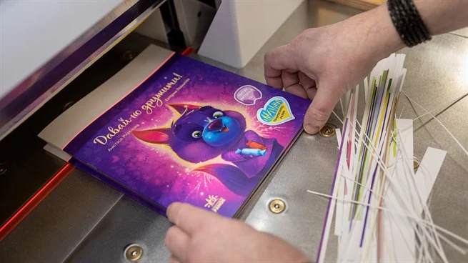 Två händer som håller i en barnbok vid en bokklipparmaskin