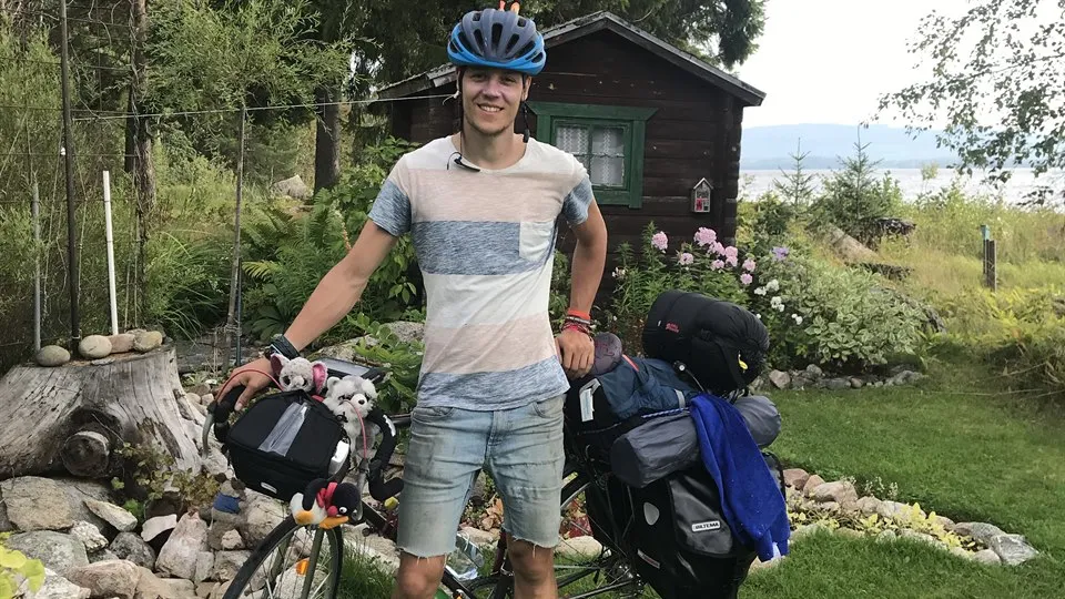 Young man stands by his fully packed bicycle