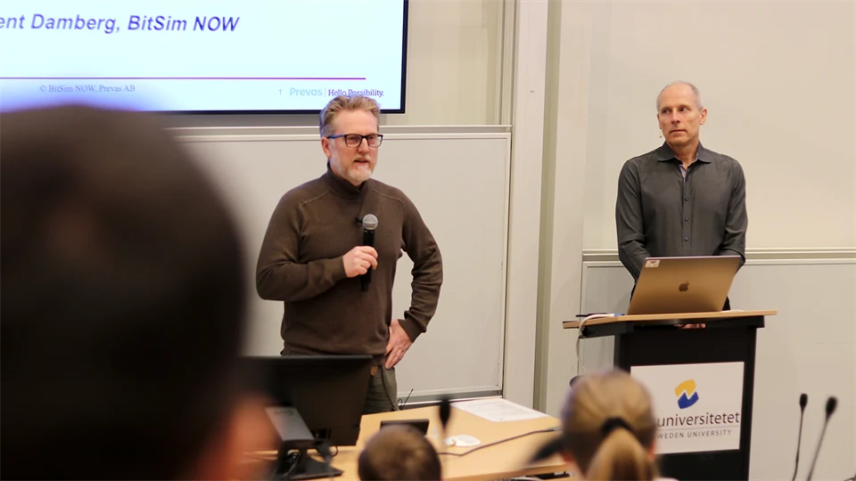 Två män står med mikrofon på scen. Publik i förgrunden. 