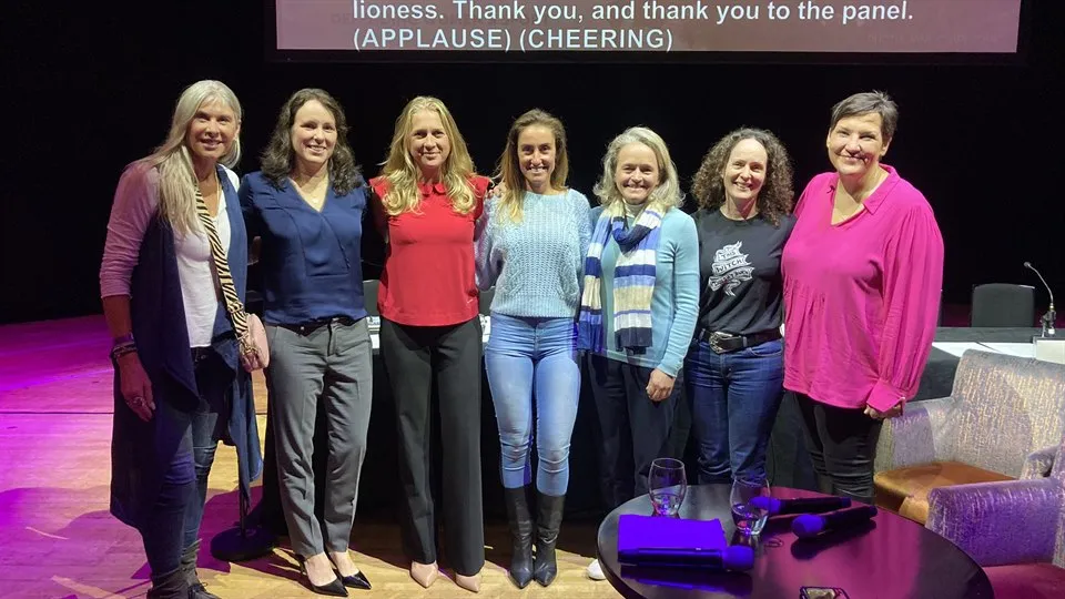 Seven women on a conference stage in front of a screen.