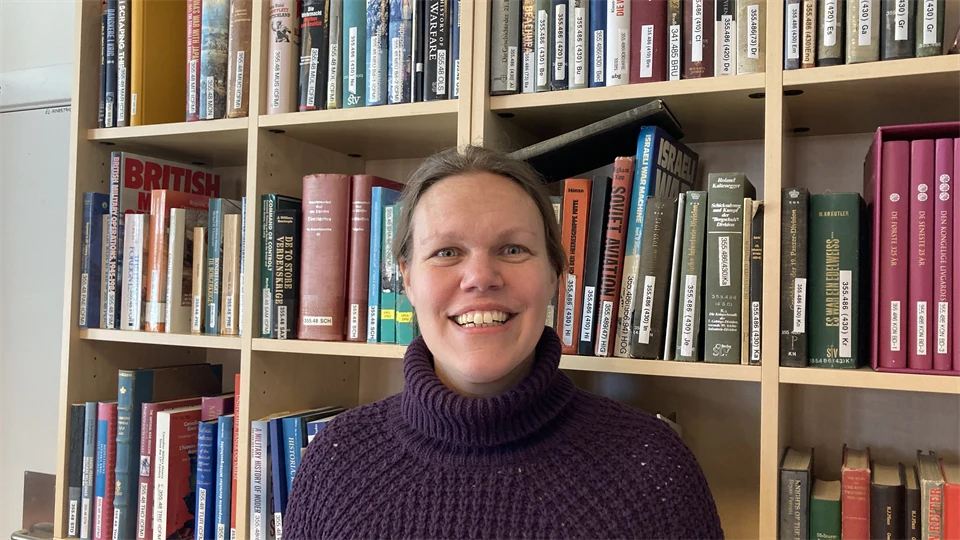 En leende kvinna står framför en bokhylla.