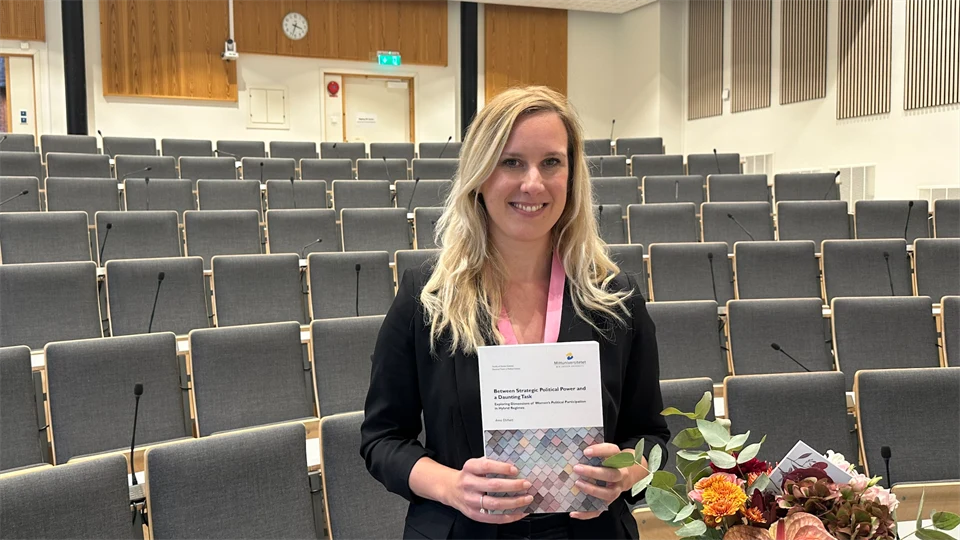 En kvinna med långt blont hår visar upp sin avhandling