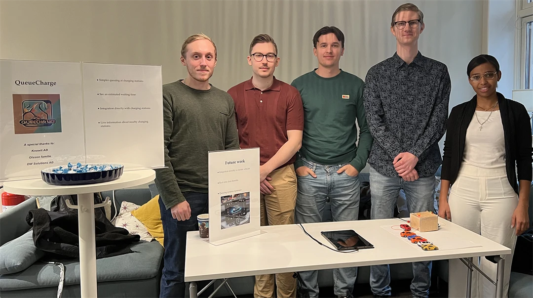 Fem personer står bakom ett bord där en prototyp på ett virtuellt kösystem för elbilsladdare ligger.