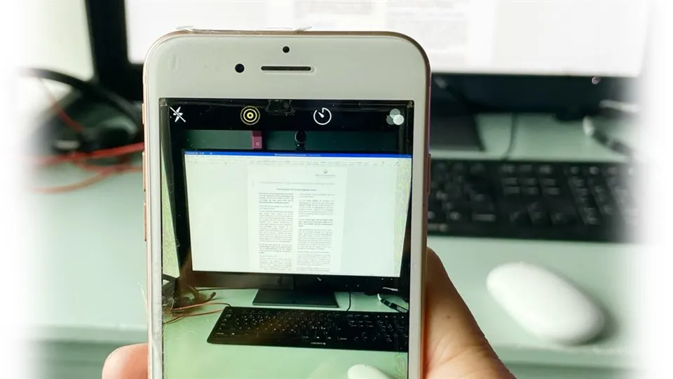 En som tar en bild av en arbetsplats med datorskärm med sin mobiltelefon.