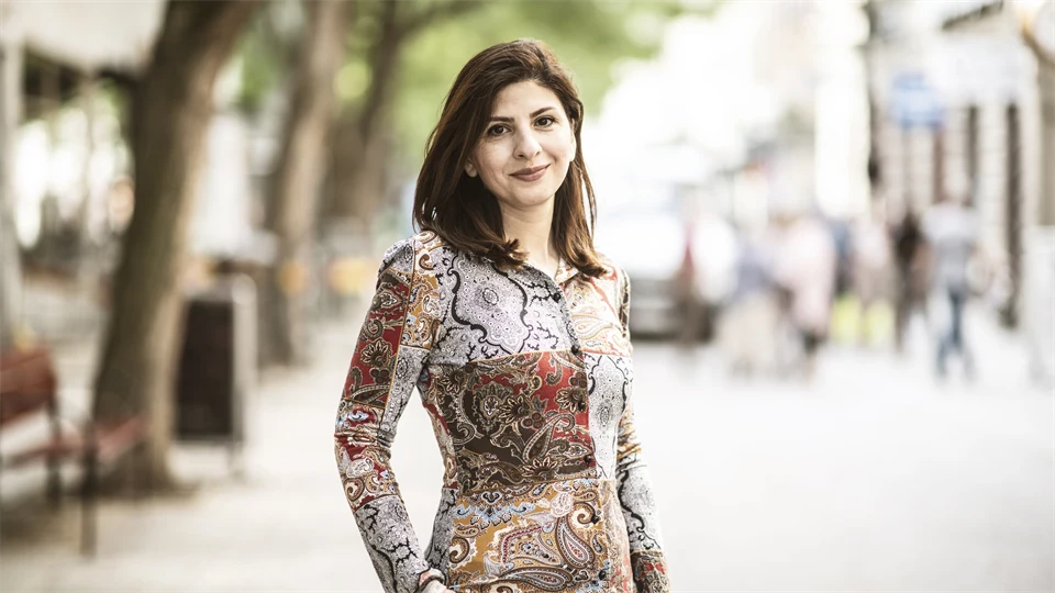 Woman with brown hair, wearing a patterned blouse, smiles at the camera