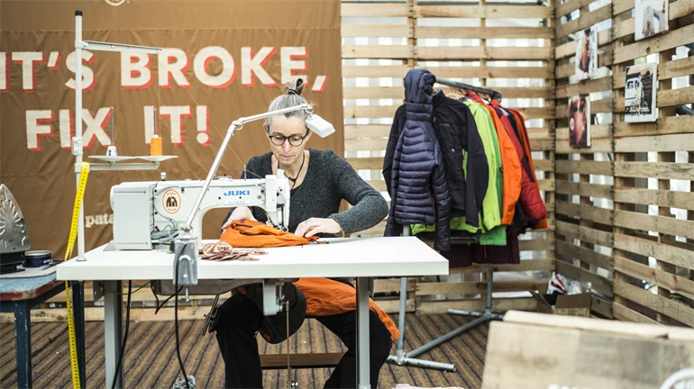 Kvinna sitter vid skrivbord och syr/lagar begagnade kläder på symaskin