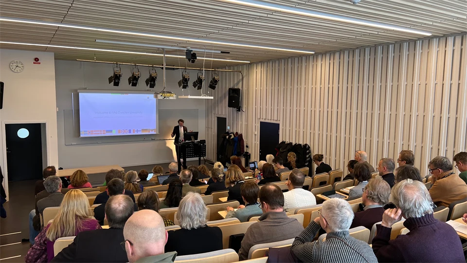 Åhörare sitter i föreläsningssal med ryggen mot kameran