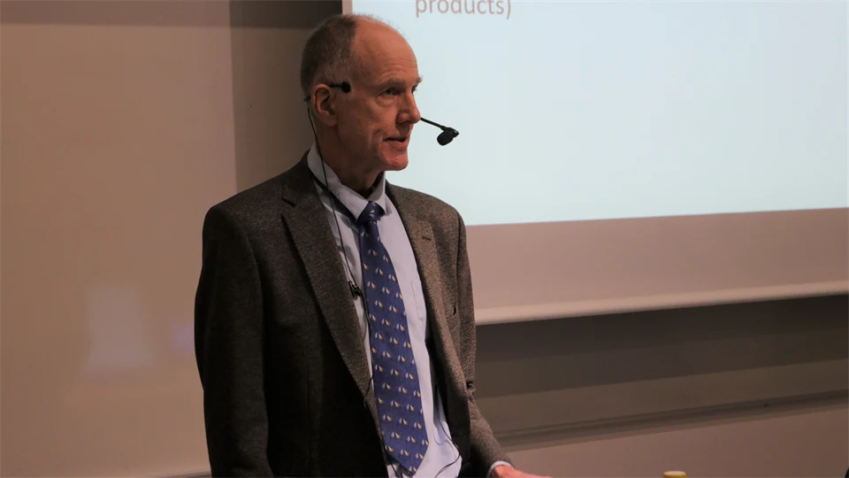 En man i kavaj och slips, med en mic som står framför en whiteboard