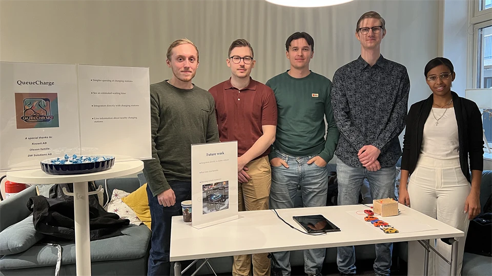 Five people stand behind a table where a prototype of a virtual queue system for electric car chargers is located.