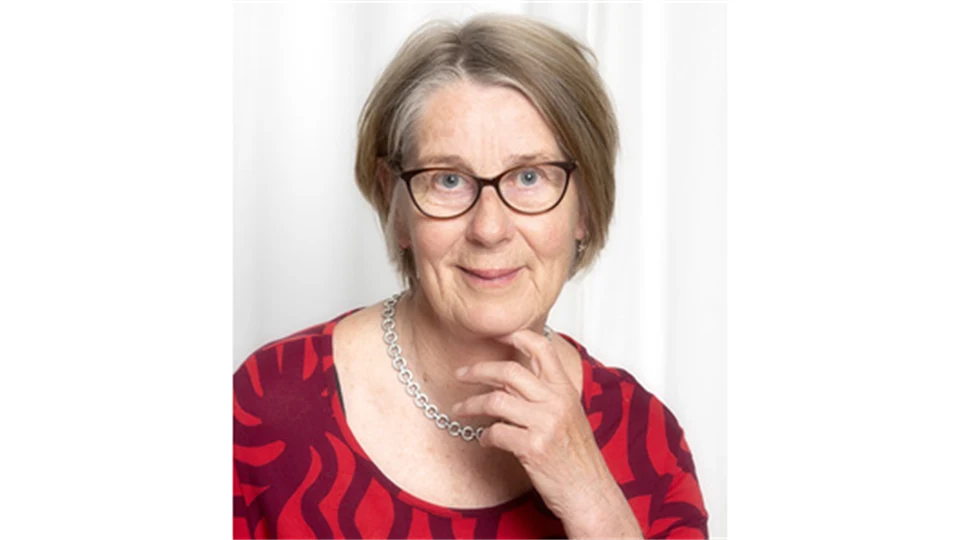 En kvinna med ljusbrun page, glasögon och ett vänligt leende klädd i en röd tröja.