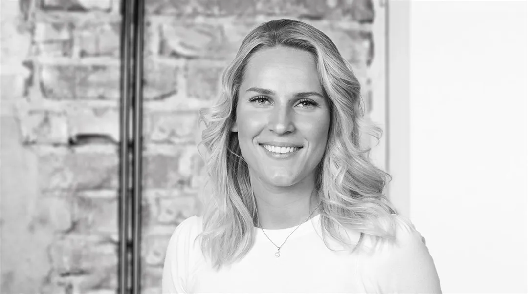 Kvinna med ena handen i fickan som står framför en tegelvägg