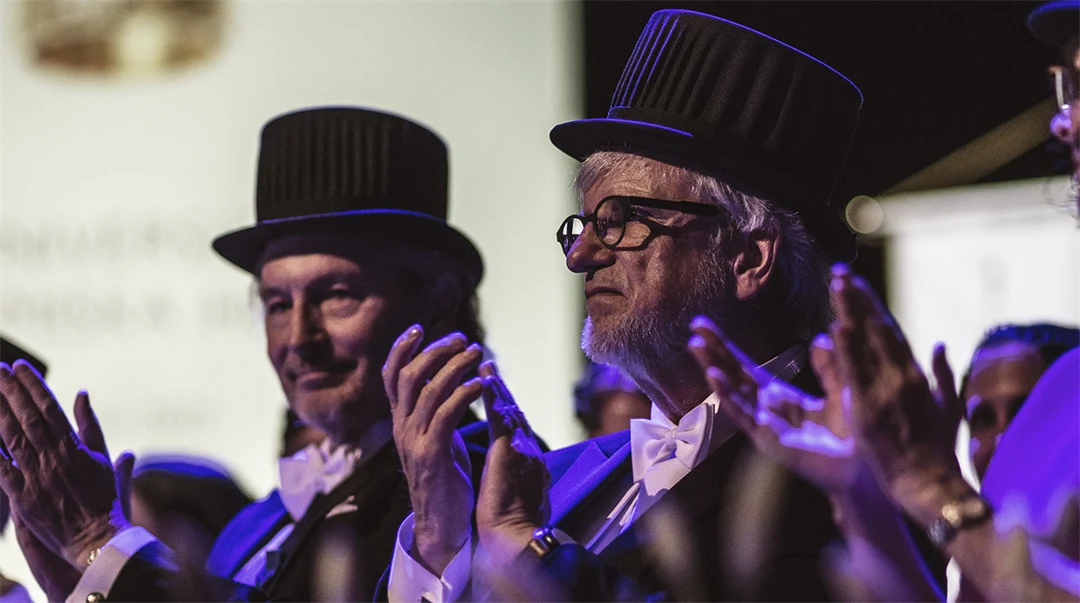 Four well-dressed people with doctor's hats clap their hands.