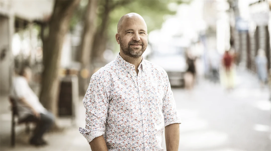 Man med ljus mönstrad skjorta ler mot kameran