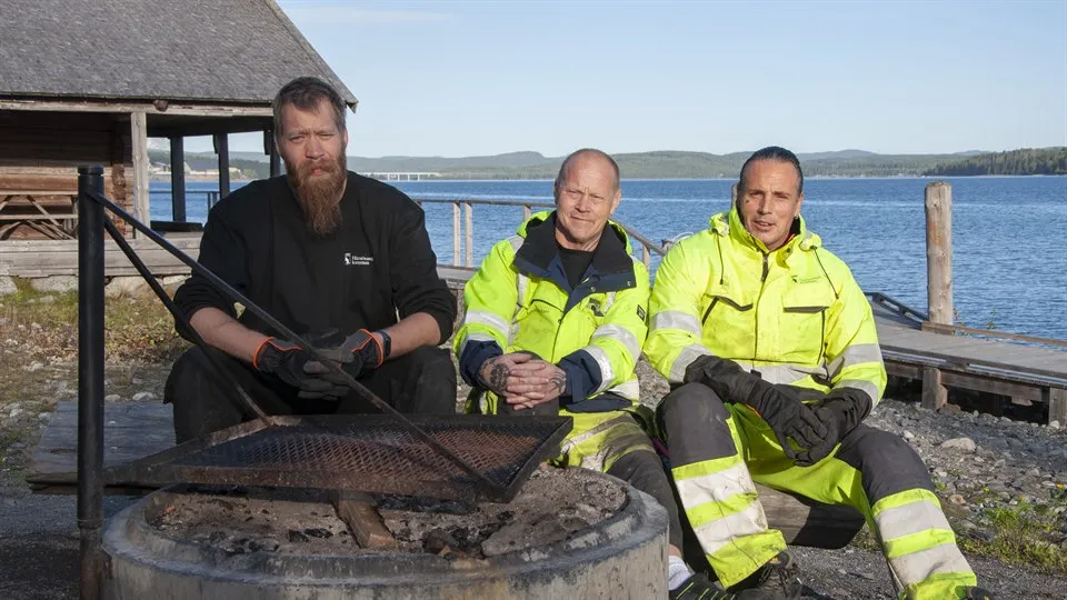 Tre personer sitter utomhus vid en grillplats.