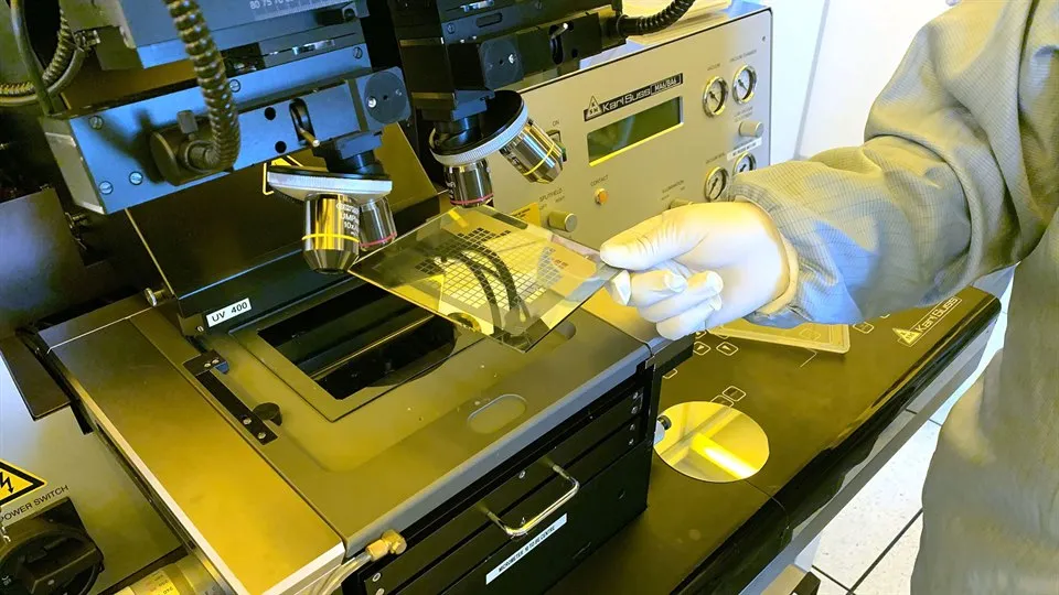Hand holding a square plate under a microscope.