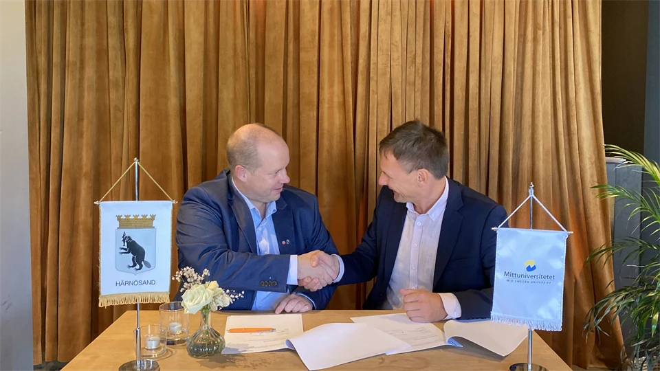 Två män sitter vid ett bord och skakar hand