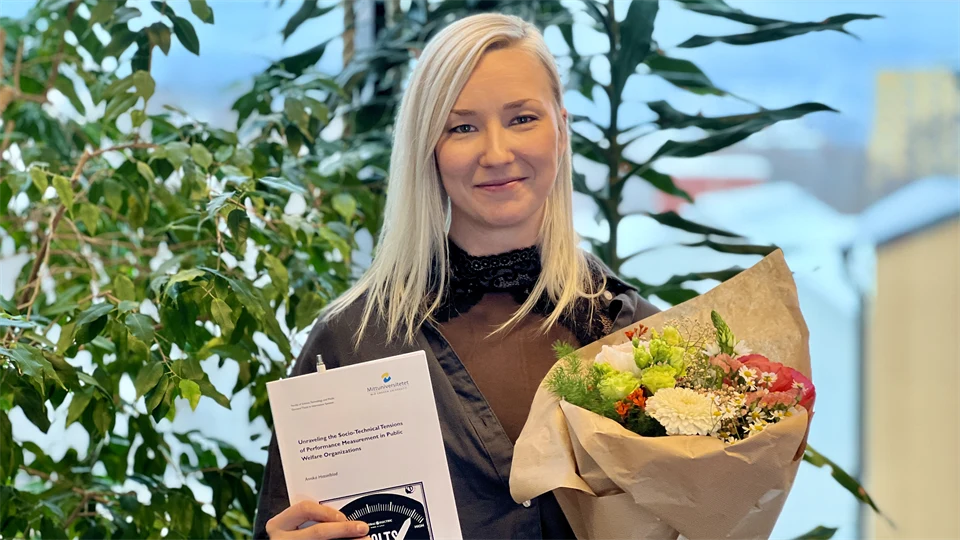 En blond kvinna håller i en bok och blommor