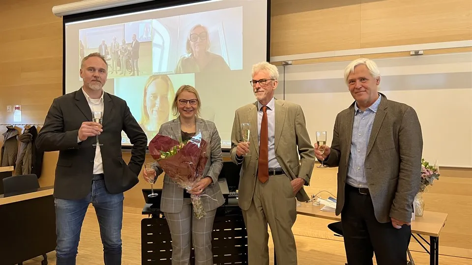 Fyra personer ståendes framför ett skrivbord med glas i handen.