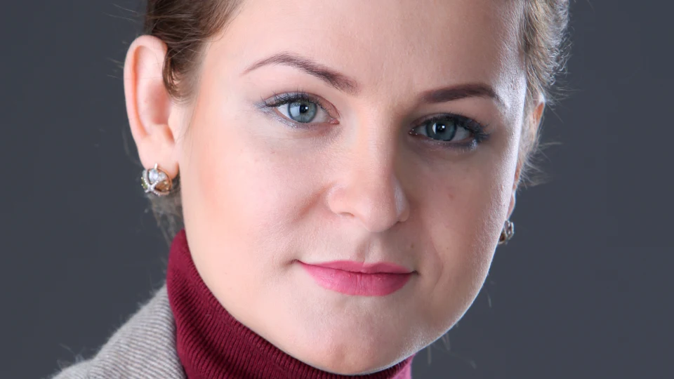 En porträttbild på en kvinna med mörkt uppsatt hår, en vinröd polotröja och grå kavaj