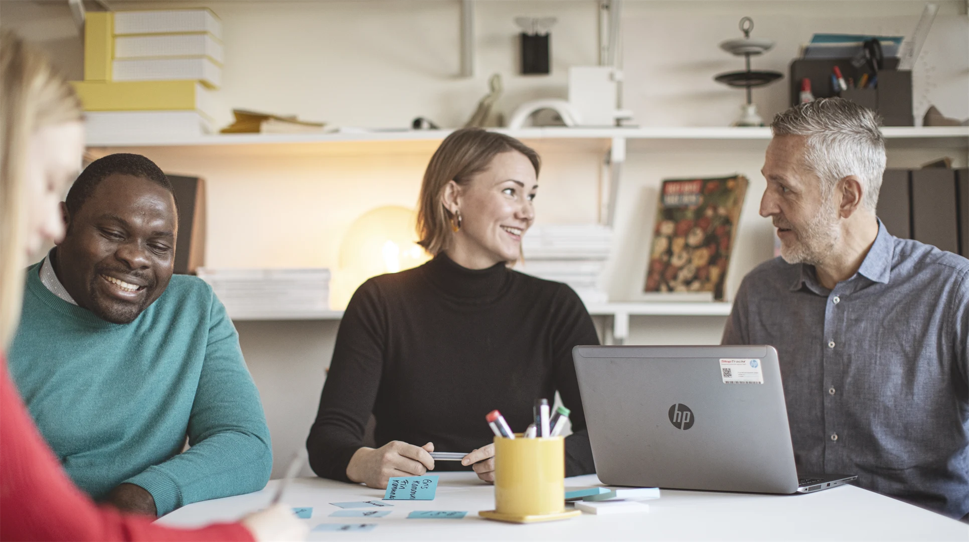 Fyra studenter runt ett bord som arbetar med en laptop och post-it lappar.