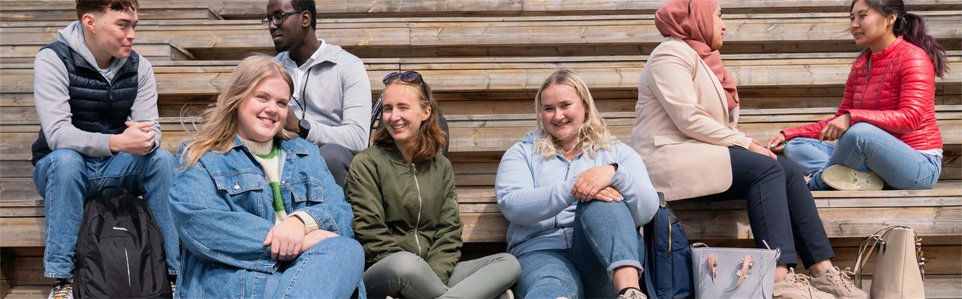 A group of students sit on a wooden staircase and talk.