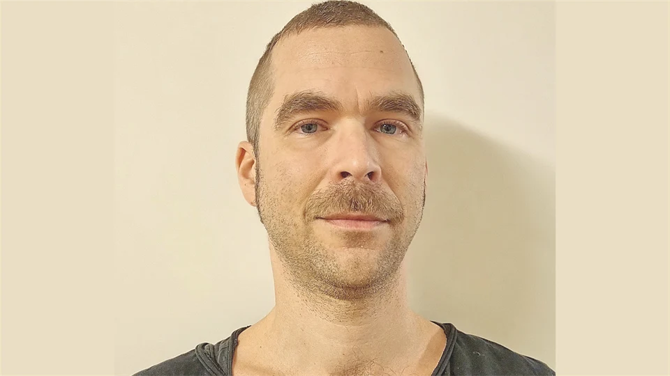 En man med snaggat brunt hår och svart t-shirt