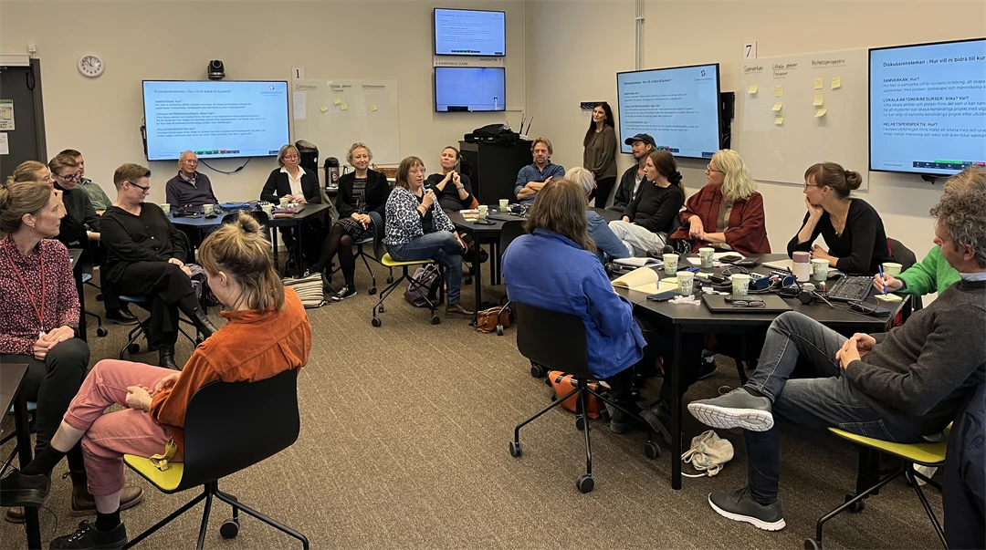 About thirty people sit at round tables in a room and talk in small groups.