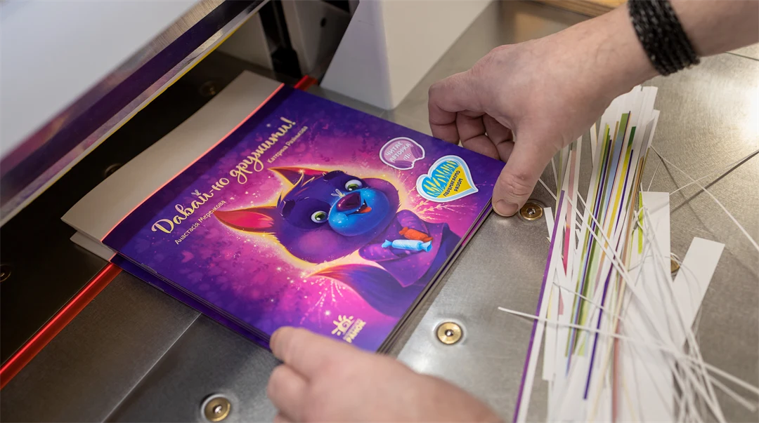 two hands holding a childrens book in a book cutter machine