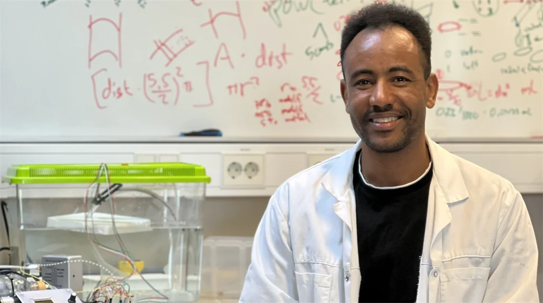 En man sittandes i labbrock framför en whiteboardtavla med massor av formler